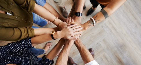A diverse group of people standing in a circle, each placing their hands together in a show of unity and teamwork.
